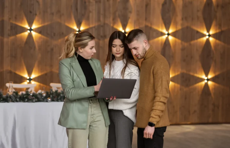 dos mujeres y un hombre de pie mirando un ordenador con la planificación en un evento corporativo