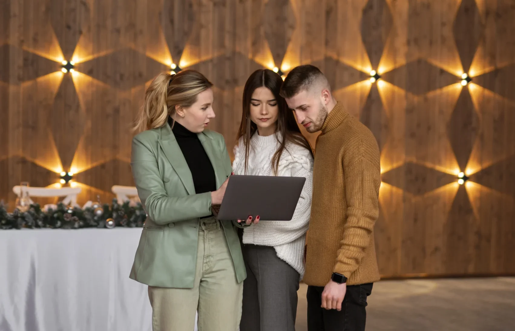 dos mujeres y un hombre de pie mirando un ordenador con la planificación en un evento corporativo